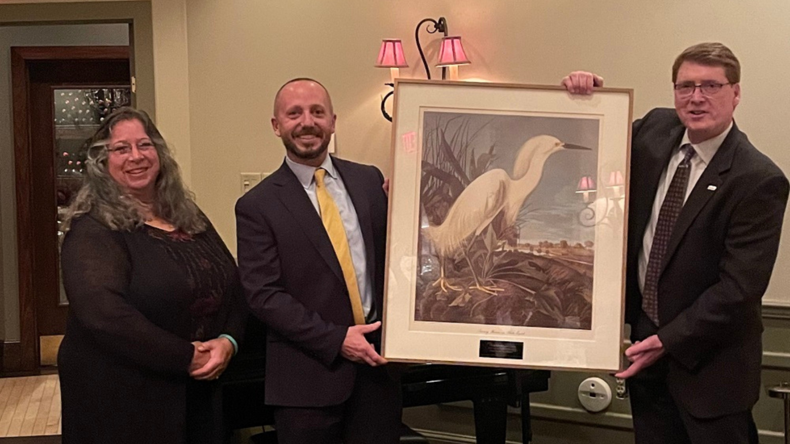 Audubon New York Executive Director Mike Burger and Board Chair of the Audubon Council Joy Cirigliano stand on either side of Commissioner Seggos, holding a large bird painting.