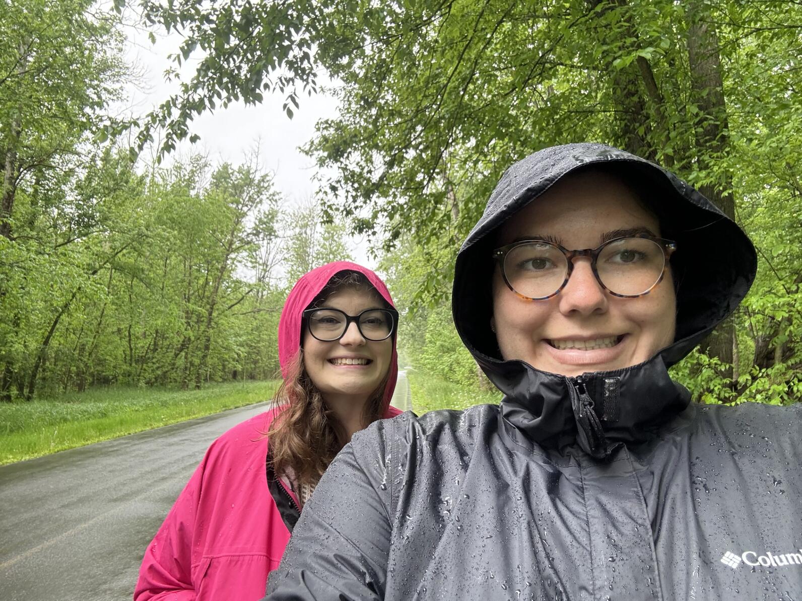 A selfie of Amanda Ives and Teresa Pietrusinski in raingear with their hoods up on a cloudy day.