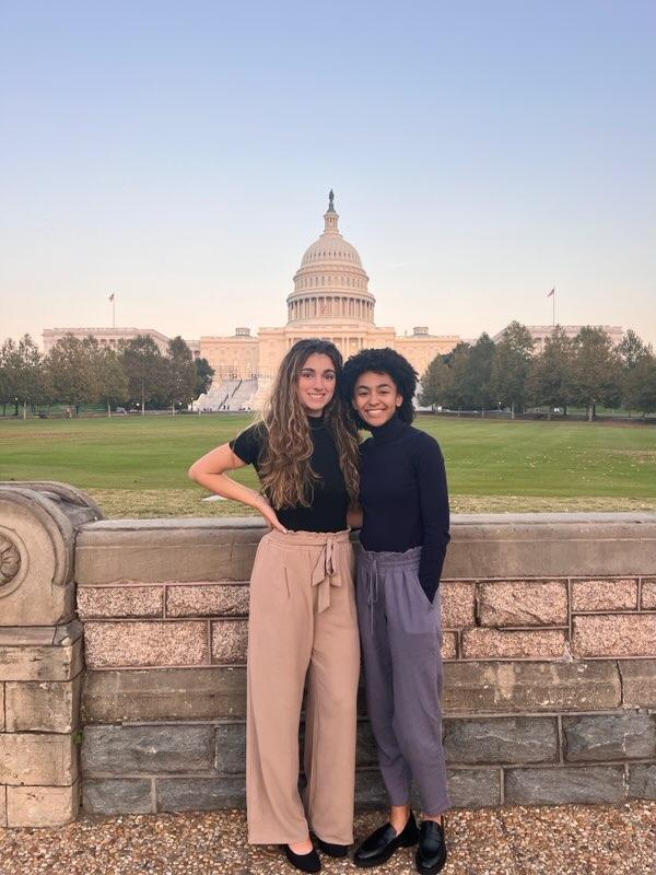 Two college aged girls stand posed together with the DC Capitol Building in the background